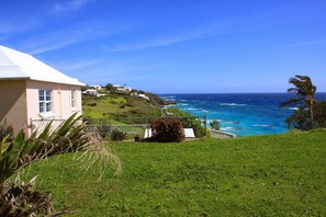 A coastal property with a view of the ocean, a grassy area, and a building with a white roof.