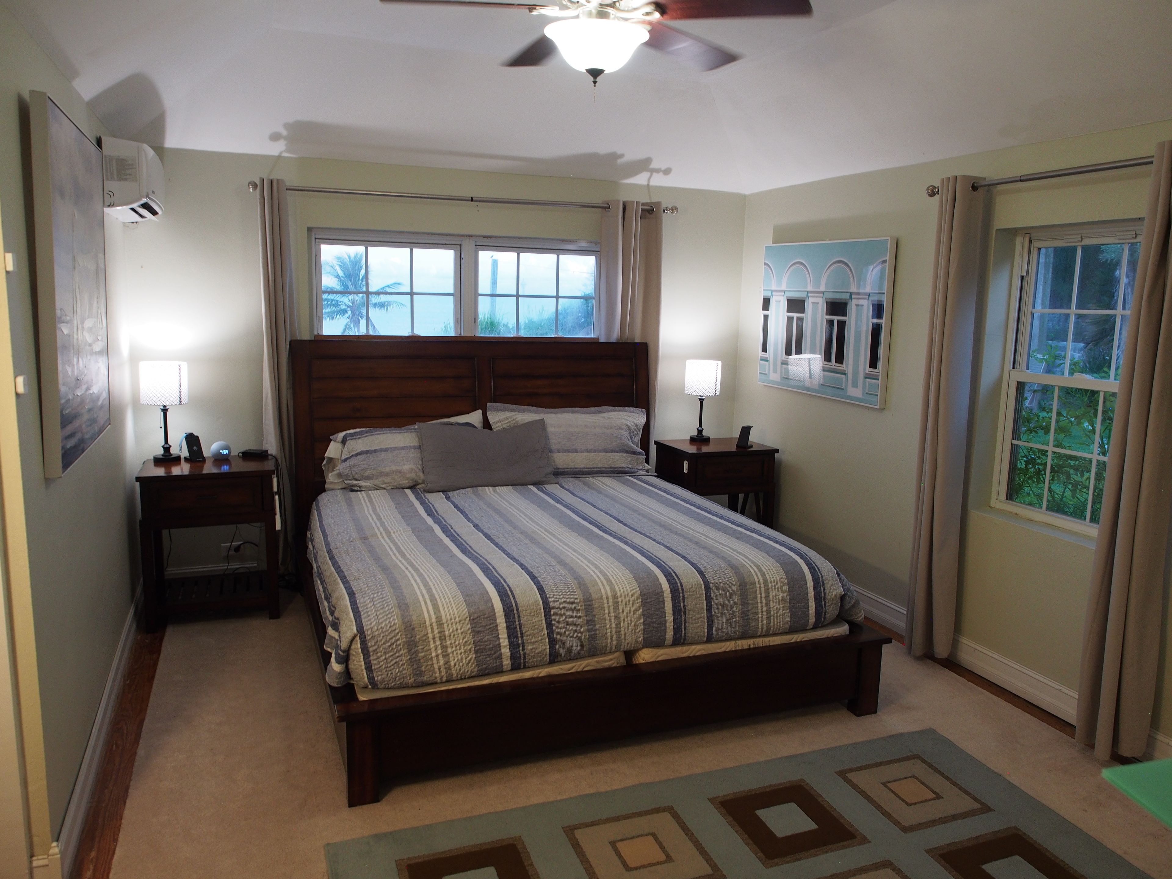 A bedroom with a bed, bedside tables, a ceiling fan, and windows.
