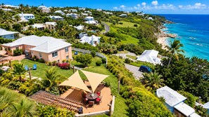 A residential area with houses, a patio with outdoor furniture, and a view of the ocean. - Spacious 3-Bedroom Bermuda Home with Spectacular Ocean Views (FL)