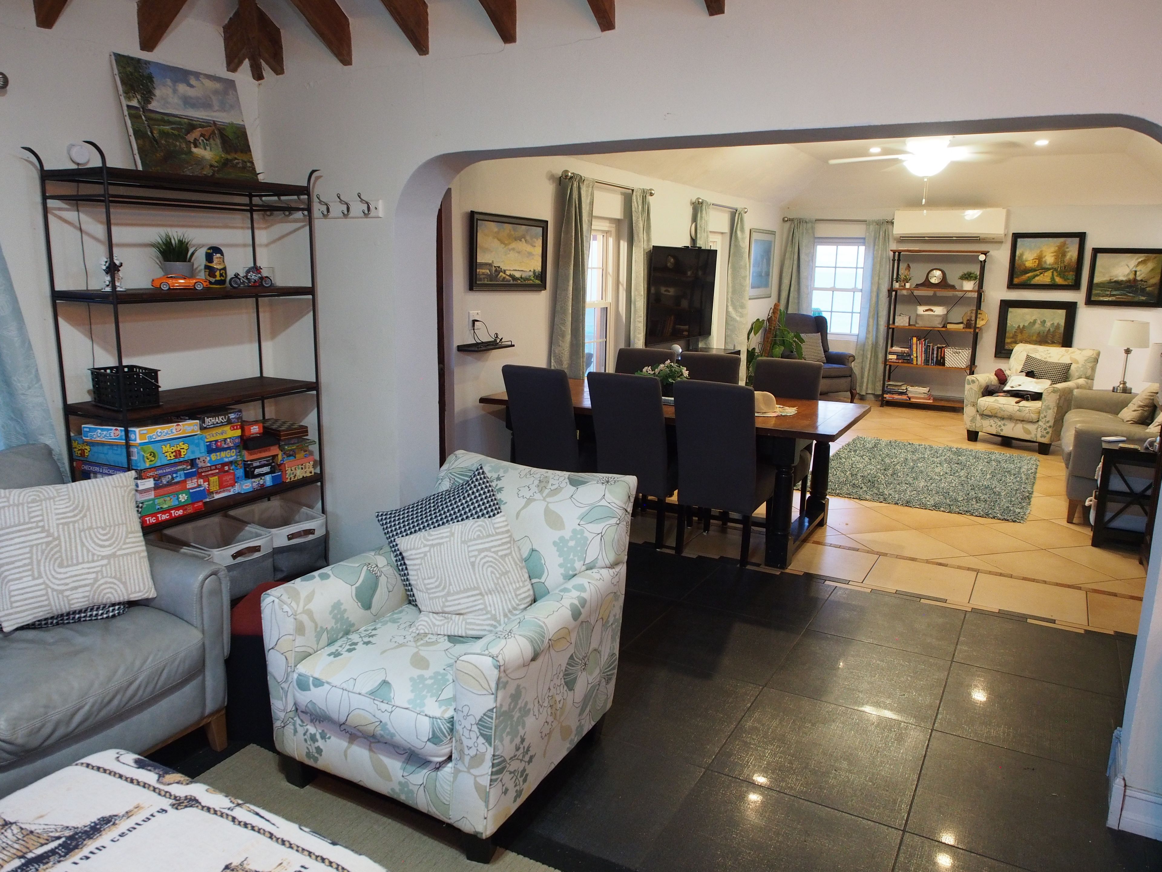 Ein Wohnzimmer mit einer Couch, einem gemusterten Sessel, einem Esstisch mit Stühlen und einem Bücherregal.