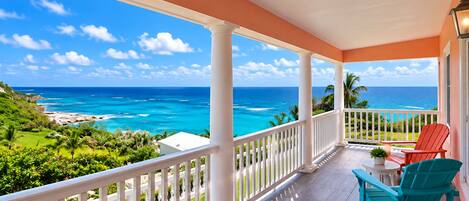 Un balcon avec vue sur l’océan, des balustrades blanches et deux chaises.