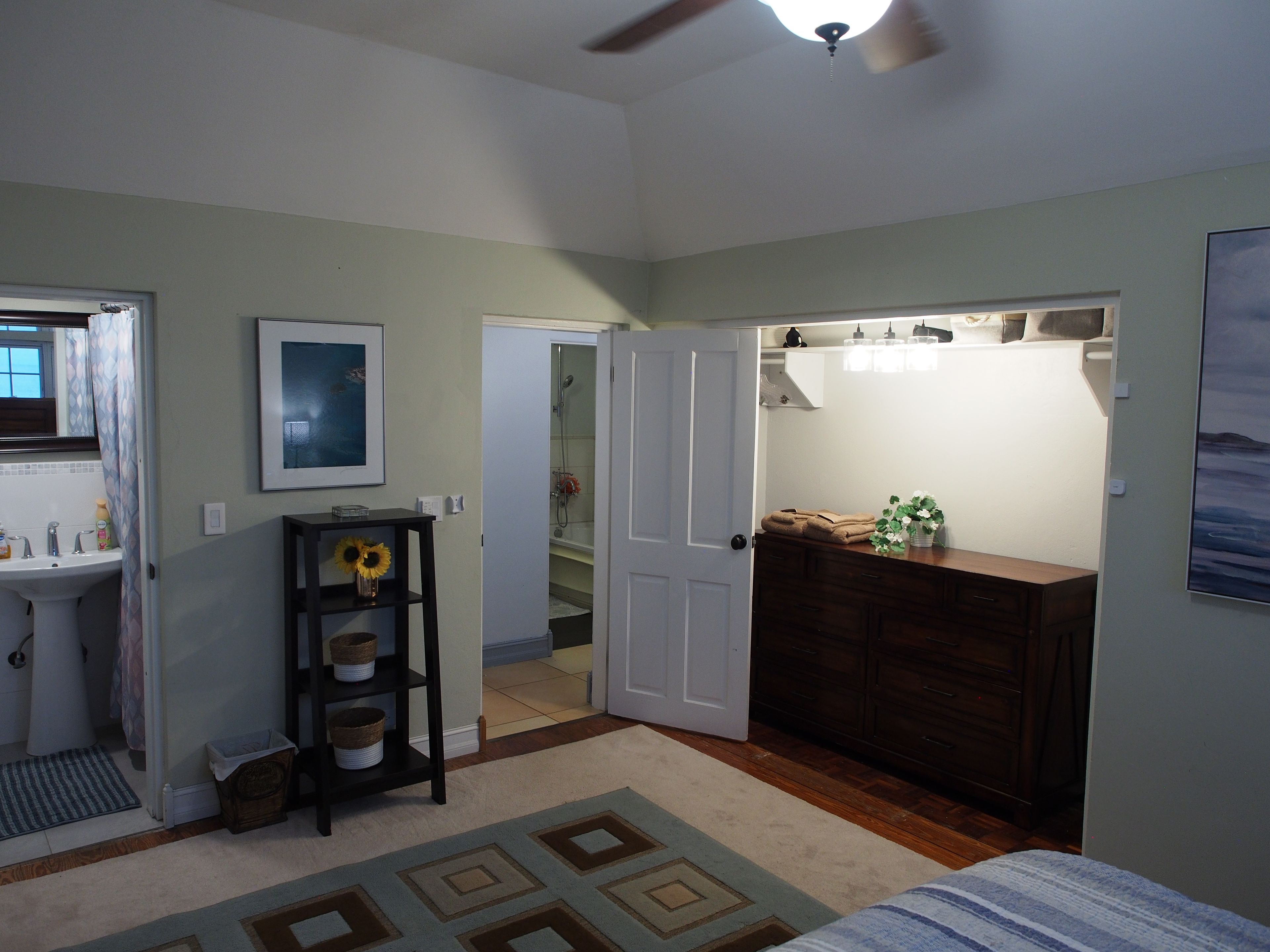 Quarto com cama, cômoda, penteadeira com espelho, chuveiro e porta que dá para outro ambiente.