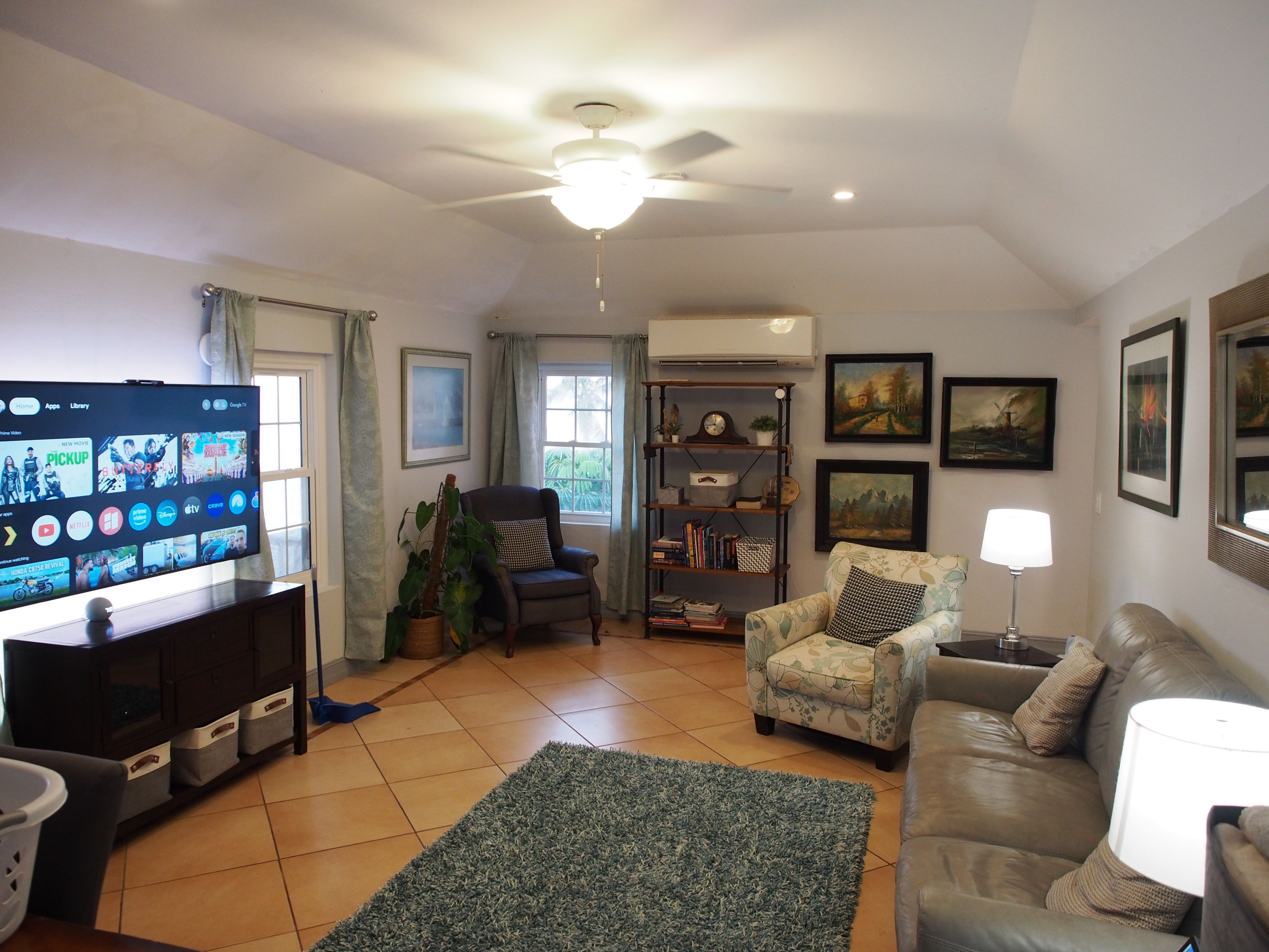 A living room with a television, a ceiling fan, a sofa, a chair, a rug, and a bookshelf.