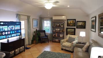 A living room with a television, a ceiling fan, a sofa, a chair, a rug, and a bookshelf.