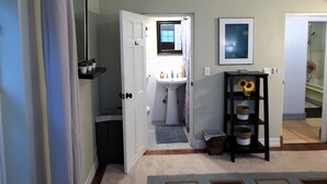 Un couloir avec une porte blanche, un lavabo, un tableau encadré et une étagère avec des paniers.