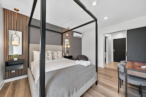 A modern bedroom with a four-poster bed, bedside tables, a desk with chairs, and a wardrobe. - The Columbus Hotel - The Reimagined Suite - 52-304 (Middletown)