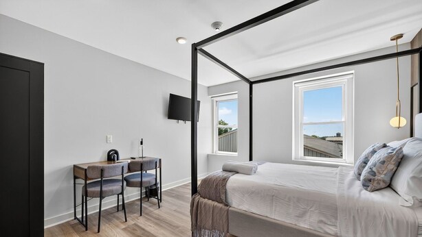 Una camera da letto con un letto a baldacchino, una scrivania con due sedie, una televisione a parete e due finestre.
