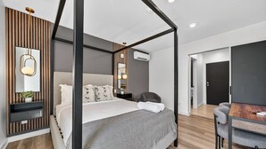 Camera moderna con un letto a baldacchino, un comodino con una lampada e vista sull'area pranzo adiacente.