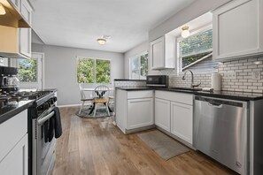 A modern kitchen with white cabinets, a stainless steel dishwasher, and a black countertop. - New! East Austin 4BR w/Fenced Yard, Patio + Dogs (Austin)
