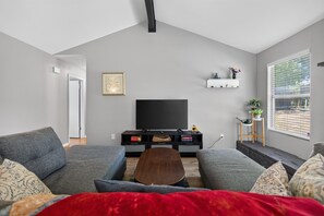 A modern living room with a flat-screen TV, grey sofas, a wooden coffee table, and a red throw blanket. - New! East Austin 4BR w/Fenced Yard, Patio + Dogs (Austin)