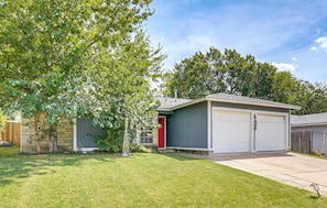 A residential garage with a red door and a grey exterior, adjacent to a house with a stone facade and a wooden fence. - New! East Austin 4BR w/Fenced Yard, Patio + Dogs (Austin)