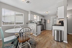 A modern kitchen with white cabinetry, a stainless steel refrigerator, and a dining area with a round table and chairs. - New! East Austin 4BR w/Fenced Yard, Patio + Dogs (Austin)