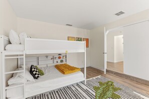 Llits superposats amb capçalera, una porta blanca i un passadís que condueix a una altra habitació.