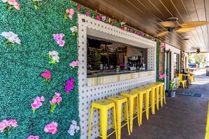 A restaurant with a green wall adorned with flowers, a counter with stools, and a ceiling fan. - 🏖️Direct Ocean View on No Drive Beach in NSB | Castle Reef 423🩱 (New Smyrna Beach)