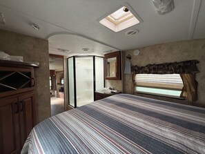 Ein Schlafzimmer mit Bett, einem Fenster mit Vorhängen, einem Badezimmer mit Waschbecken und einem Spiegel.