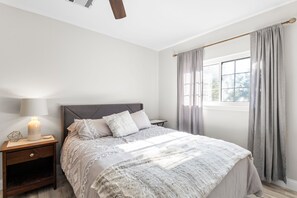 Ein Schlafzimmer mit einem Bett, Nachttischen, einer Lampe und einem Fenster mit Vorhängen.