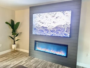 A modern living room with a mounted flat-screen TV and a built-in fireplace. - New Lux Large Modern House 15min to ATX & Airport (Austin)