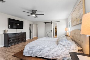A bedroom with a bed, dresser, ceiling fan, and a TV mounted on the wall. - New Lux Large Modern House 15min to ATX & Airport (Austin)