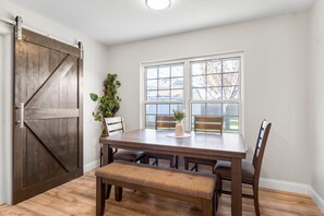 A dining area with a wooden table, four chairs, a bench, and a large window with a view of trees. - New Lux Large Modern House 15min to ATX & Airport (Austin)