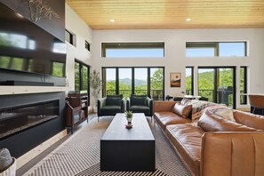 Un salon moderne doté d’une cheminée, d’un canapé en cuir et de grandes fenêtres offrant une vue sur l’extérieur.