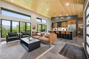 A modern living space with a large sofa, a coffee table, and a kitchen area with bar stools. - The Laurel & Sky ~ Smoky Mountains (Bryson City)