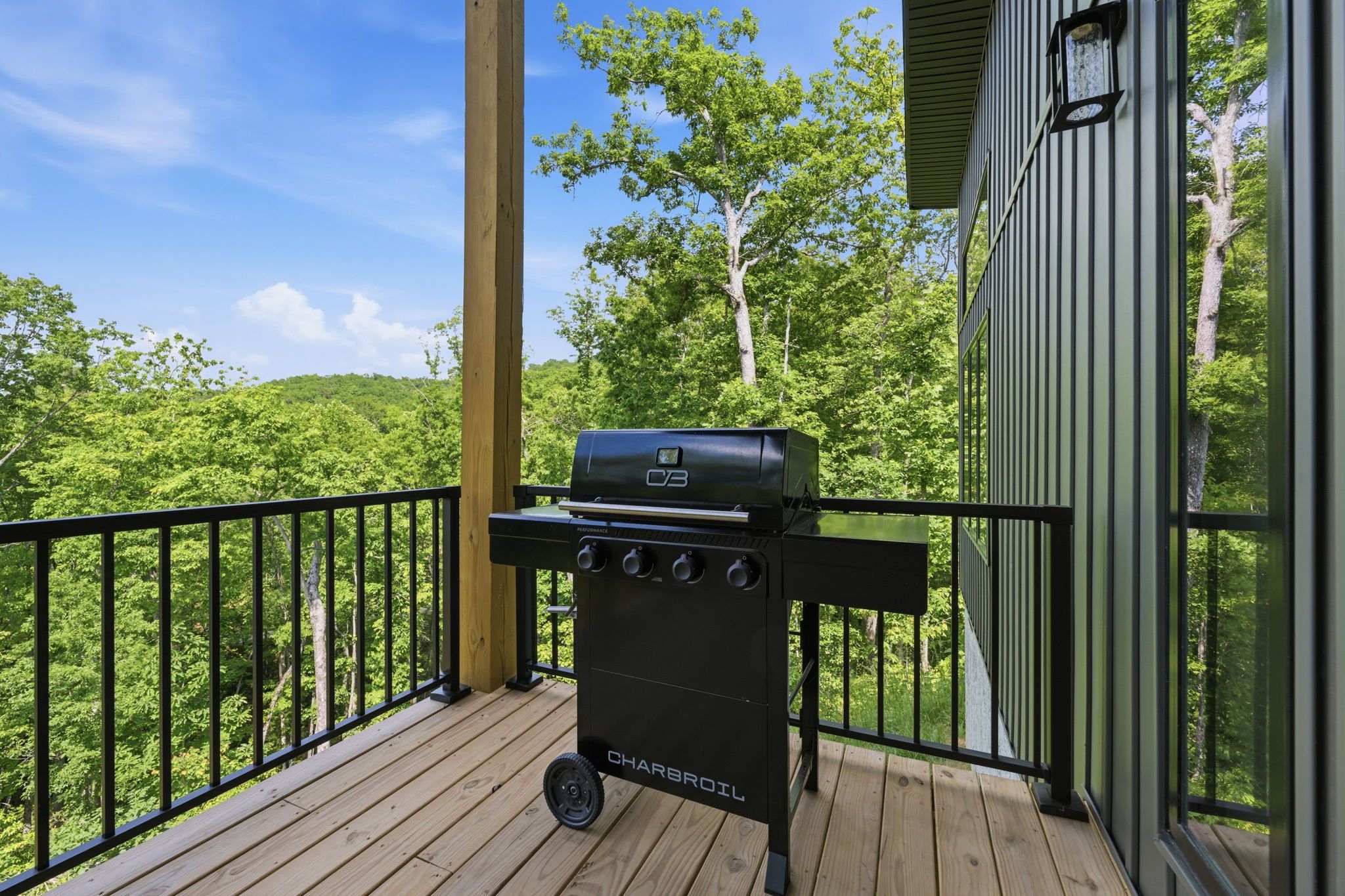 Ein Holzkohlegrill auf einer Holzterrasse mit Blick auf einen Wald.