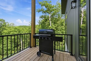 Un barbecue au charbon de bois sur une terrasse en bois, avec vue sur une forêt.