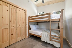 Ein Stockbett mit Holzrahmen und weißer Bettwäsche, ein mehrtüriger Kleiderschrank aus Holz sowie eine geneigte Decke mit Holzbalken.