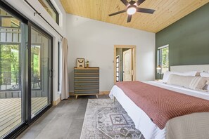 Quarto com cama, cômoda, ventilador de teto e vista por uma porta de vidro.