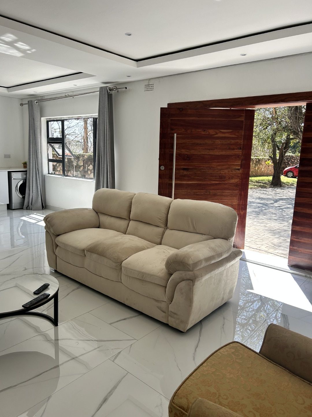 A modern living room with a beige sofa, a coffee table, and a view of the outdoors through a large window.