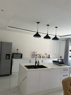 A modern kitchen with a central island, white cabinetry, and pendant lighting. -  Umhlanga   2 bedroom, 2 bathroom (Bulawayo)