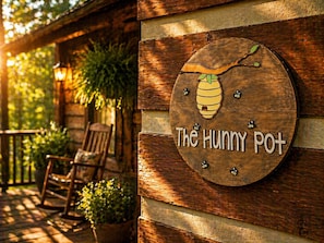A wooden sign with a bee and the text 'The Hunny Pot' on a rustic wall. - 2-bedroom secluded, romantic cabin in Sevierville. Rest,relax and unwind. (Sevierville)