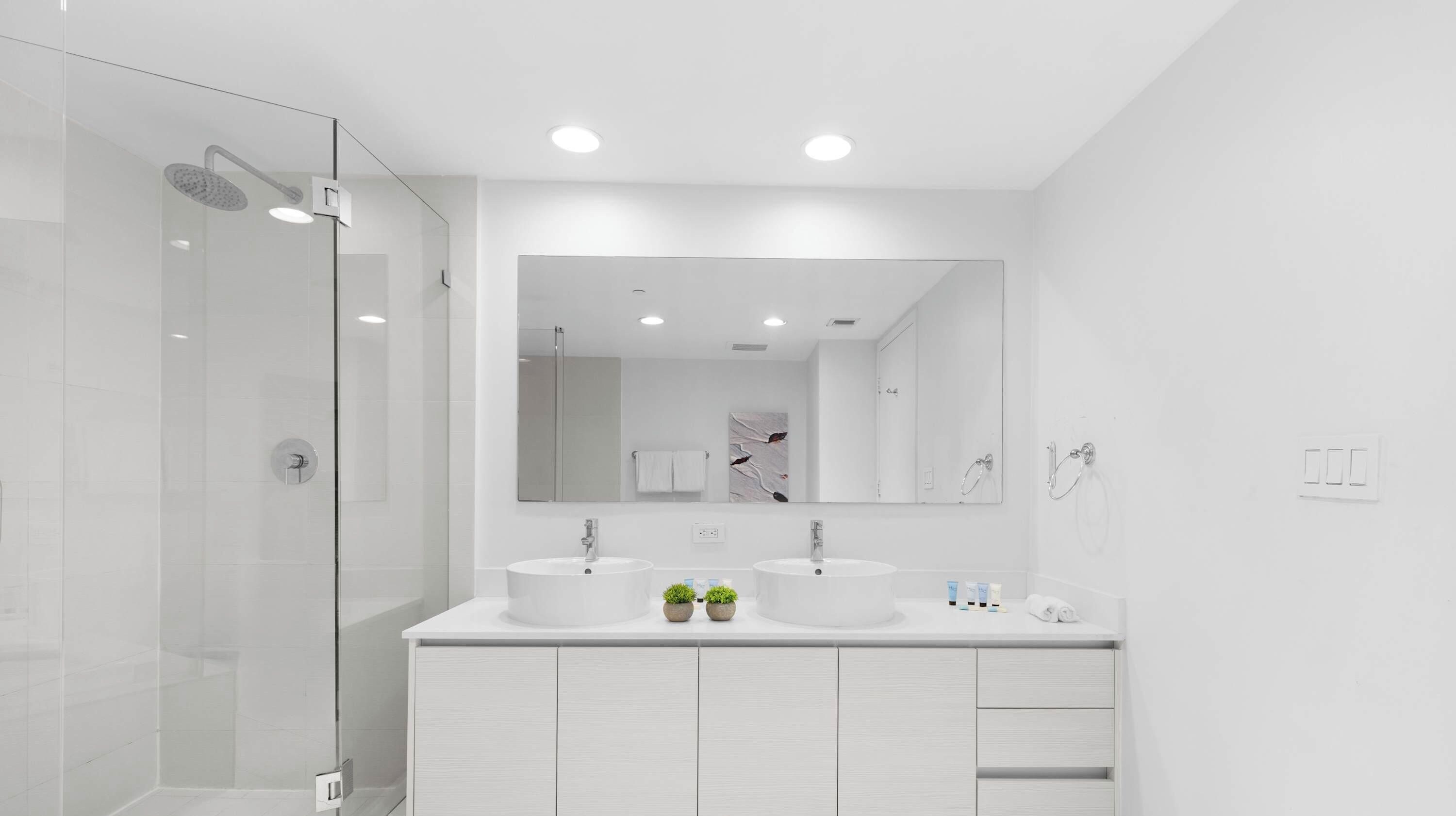 A modern bathroom with two sinks, a large mirror, and a glass shower enclosure.