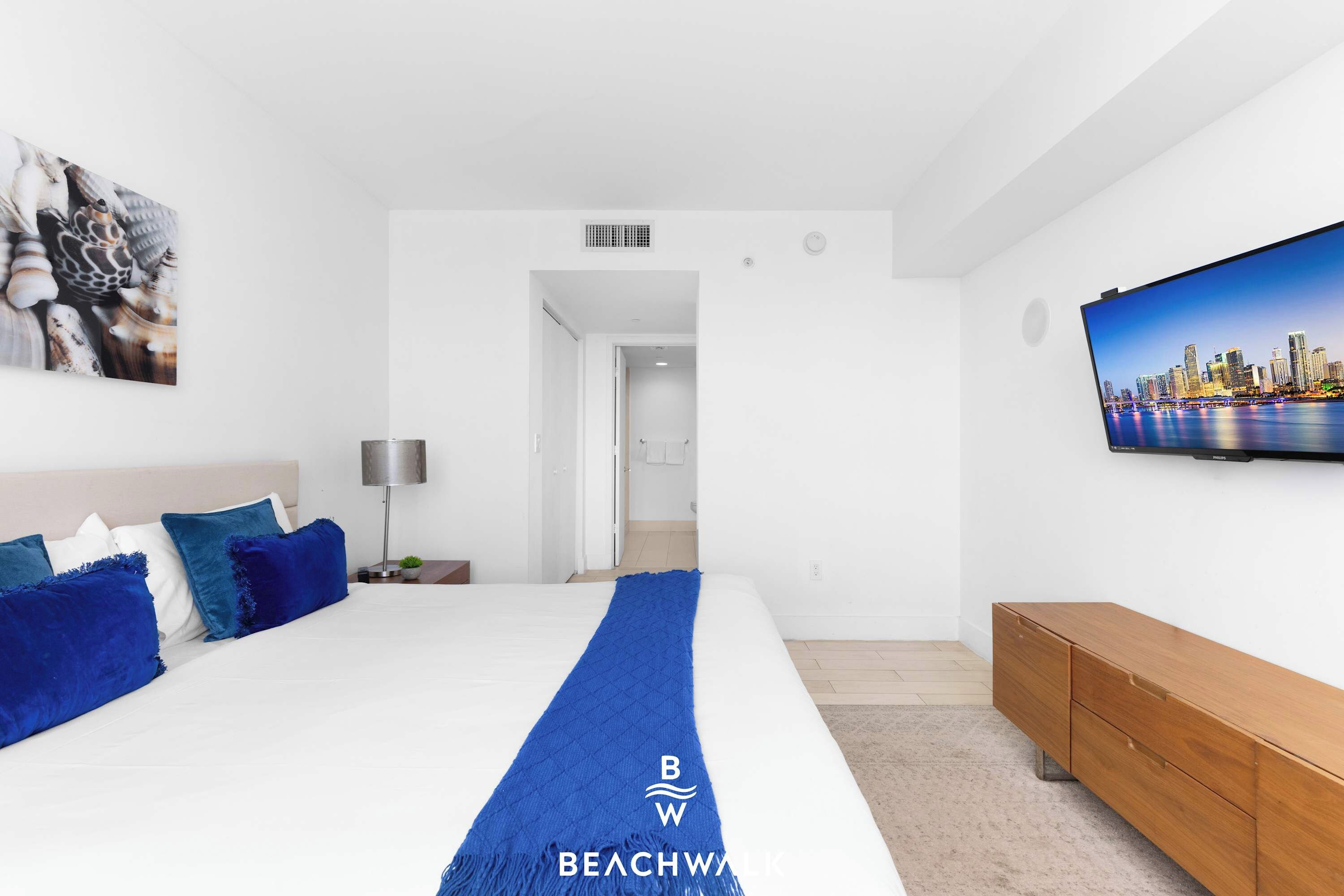 Habitación de hotel con cama, televisión, un cuadro y vistas a un paisaje urbano.