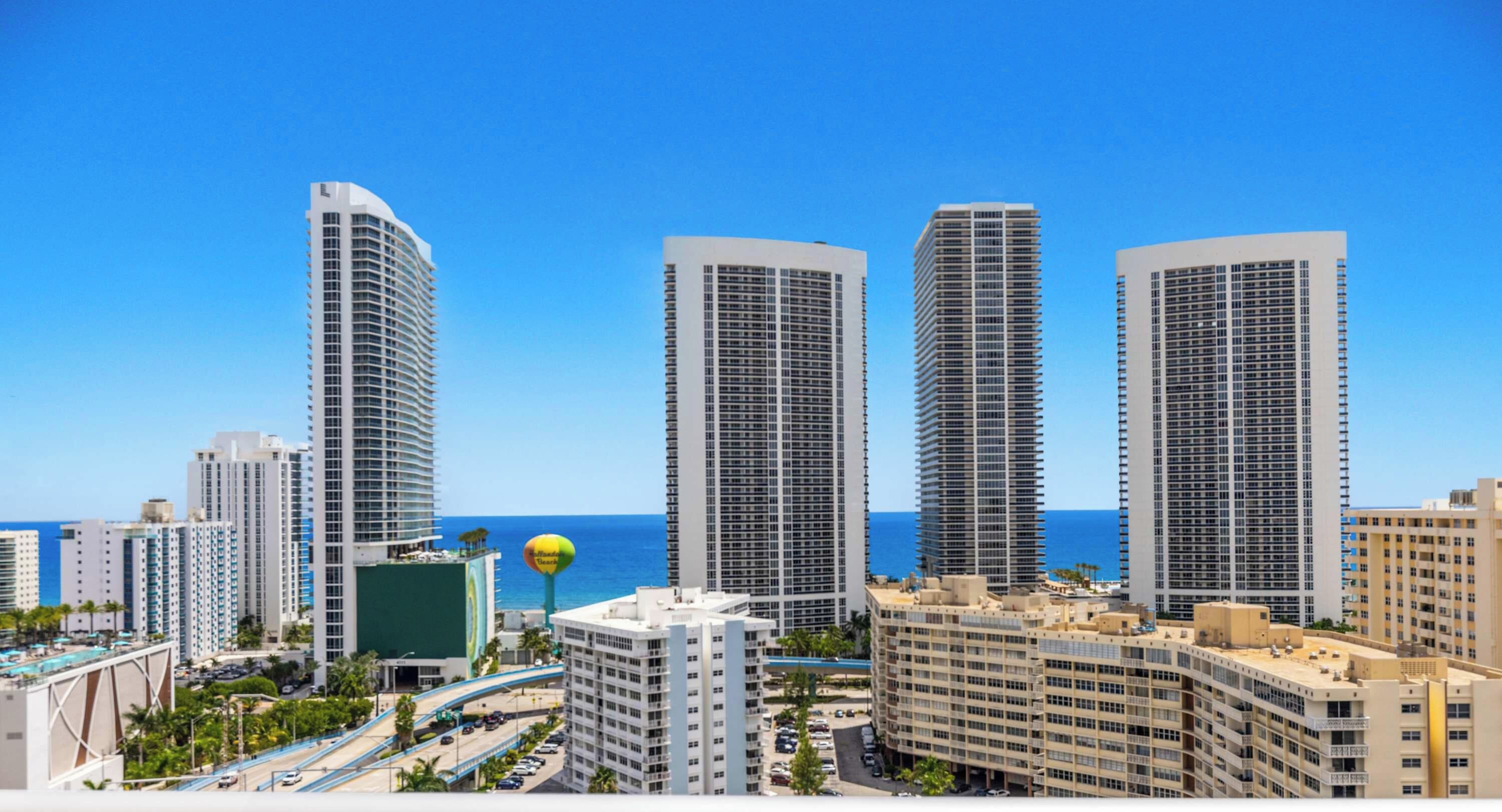 A cityscape with high-rise buildings, a clear blue sky, and a view of the ocean.