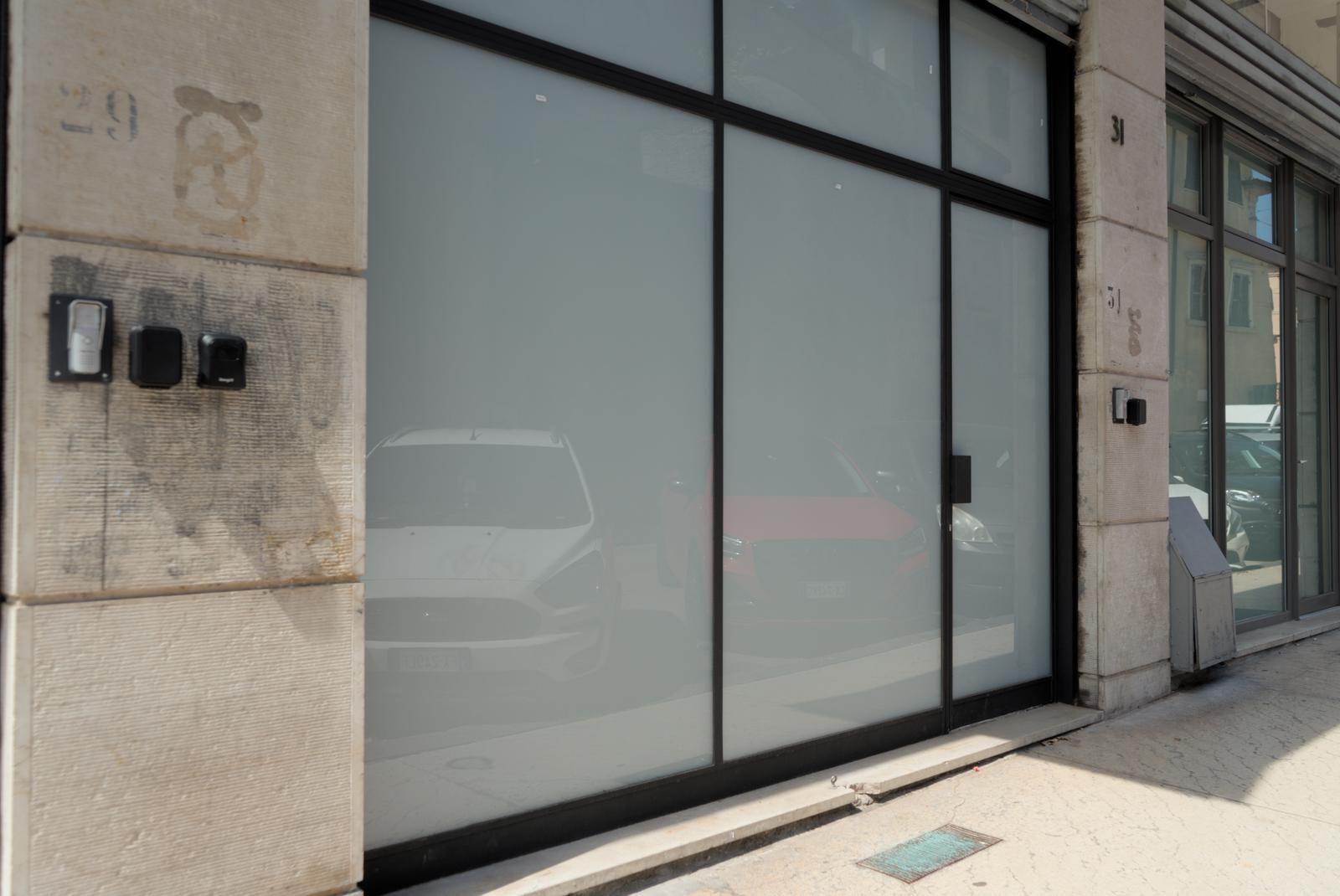 A building facade with large glass doors, a metal frame, and a concrete wall with visible wear.