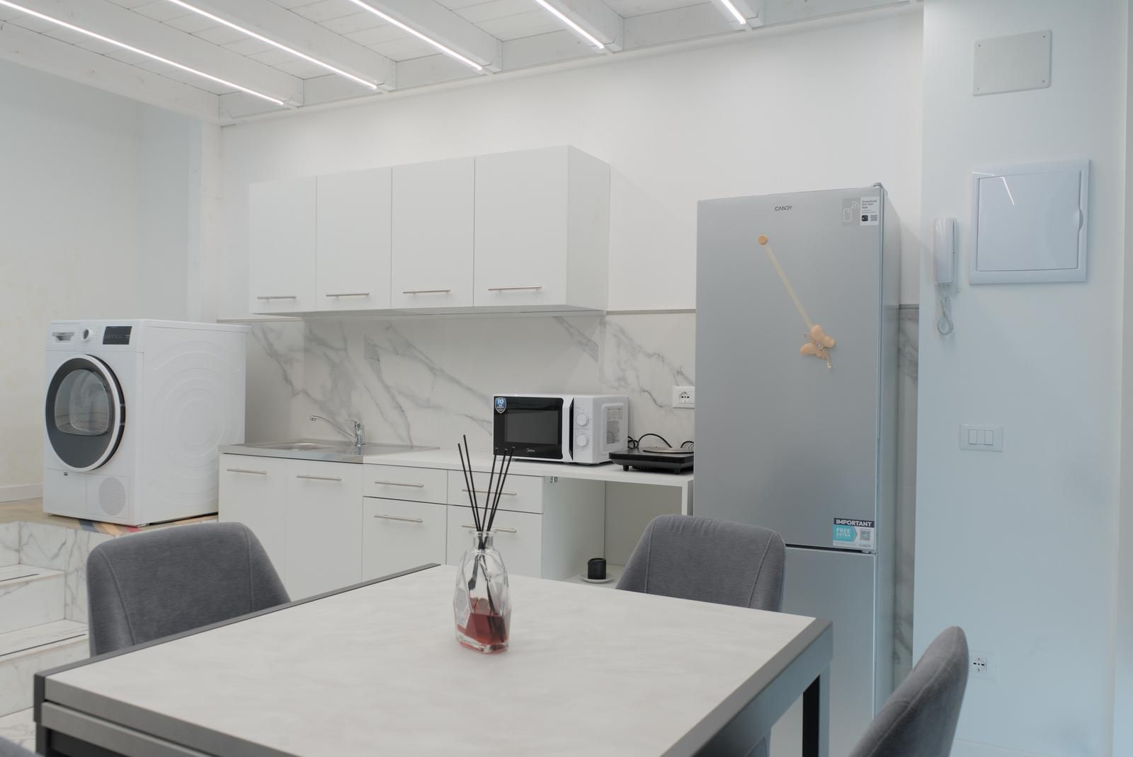 Una cocina moderna con armarios blancos, lavadora integrada, microondas y refrigerador.