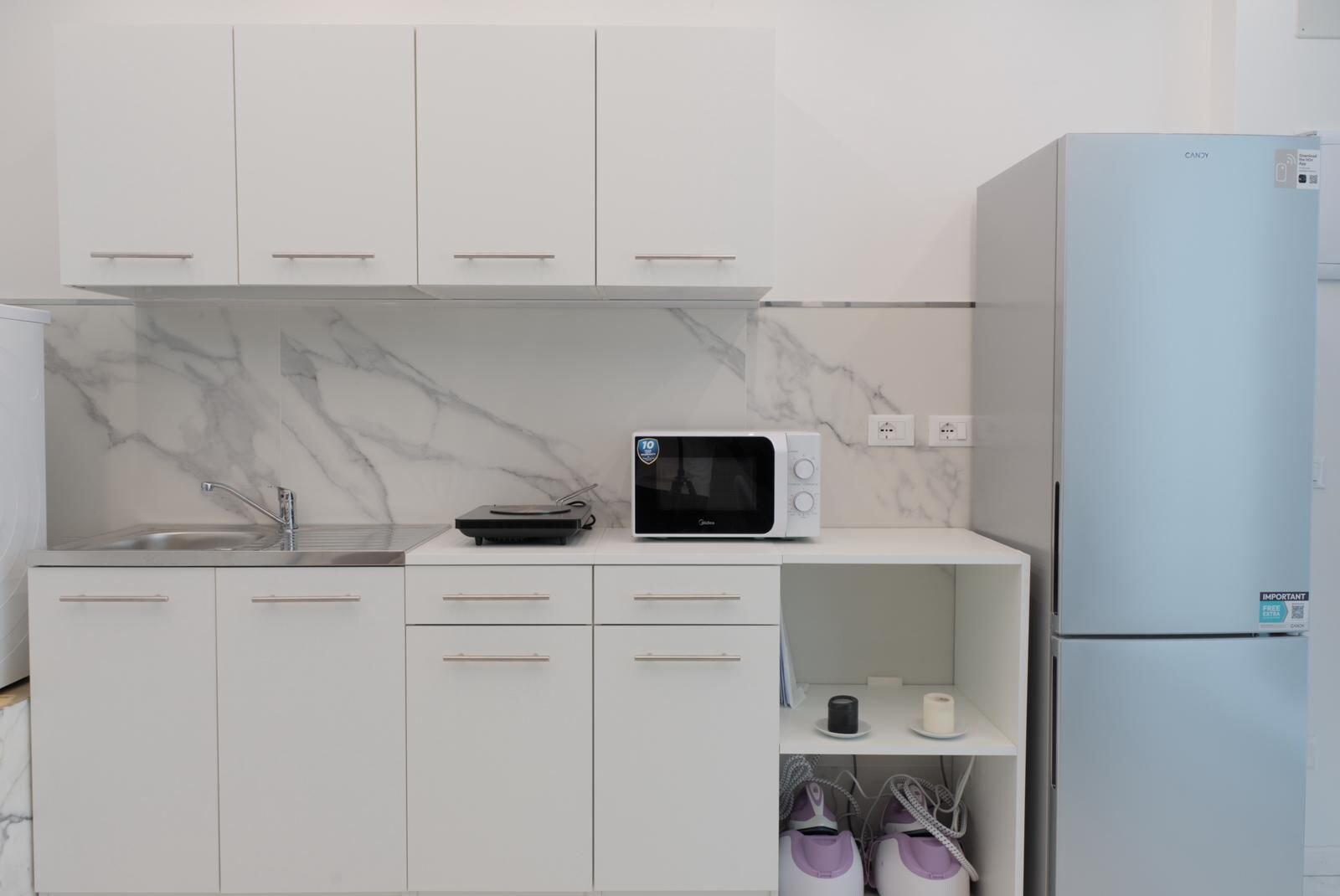 A modern kitchen with white cabinets, a microwave, a sink, and a refrigerator.
