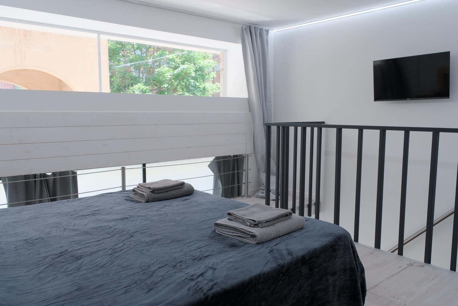 A hotel room with a bed, a TV mounted on the wall, and a balcony with a railing.
