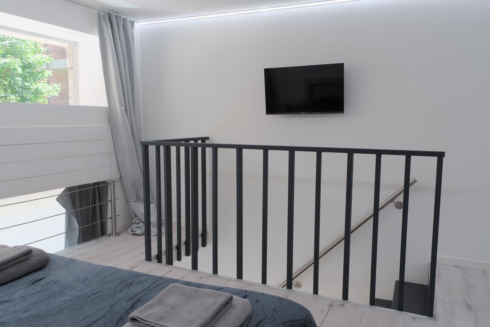 Une chambre moderne dotée d’un balcon, d’un téléviseur à écran plat fixé au mur et d’une rambarde en métal.