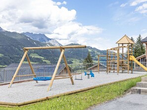 Ein Spielplatz mit Schaukeln und einer Kletterkonstruktion, vor einer Bergkulisse.