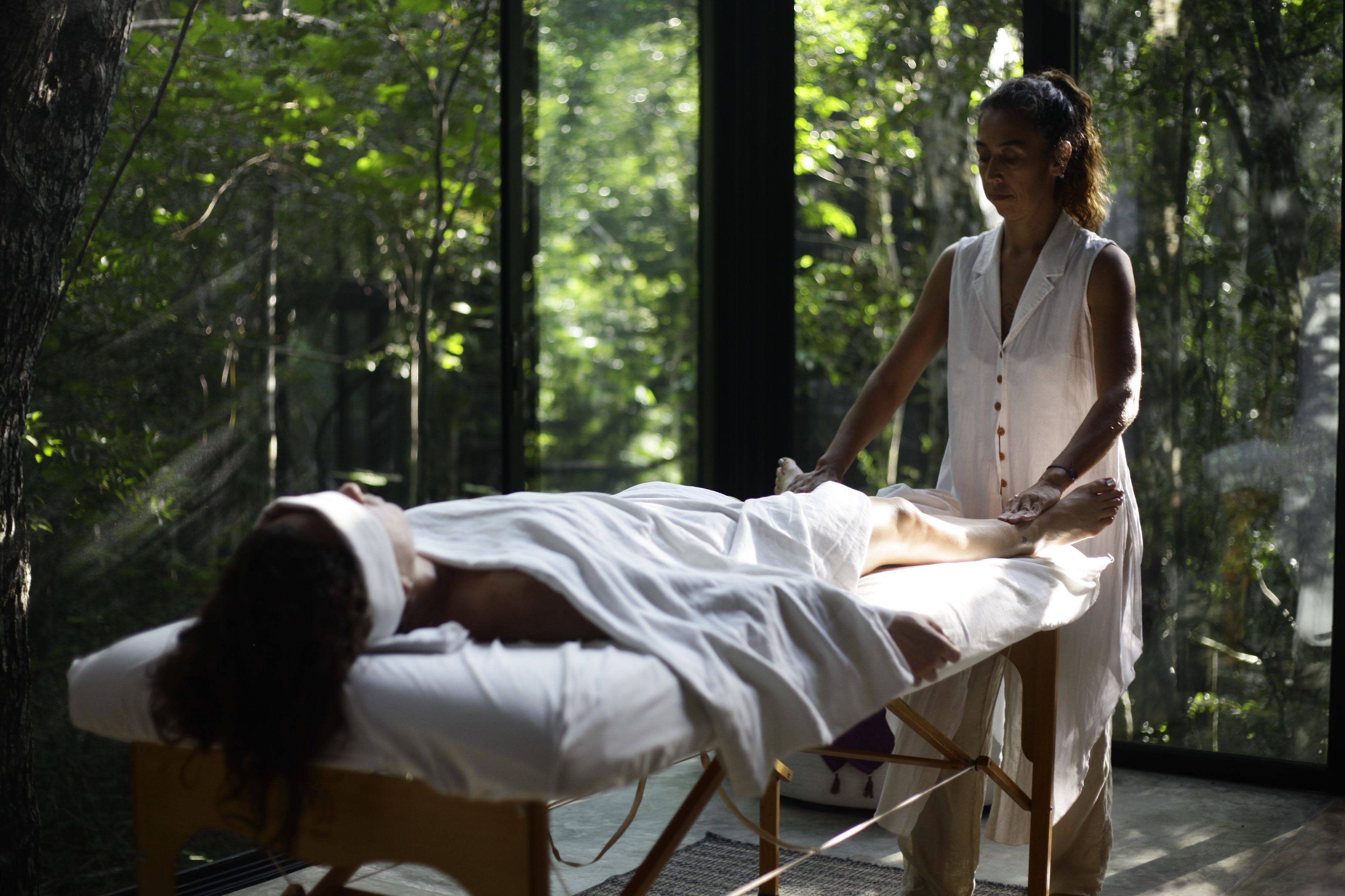 A person lying on a bed in a room with a view of a forest.