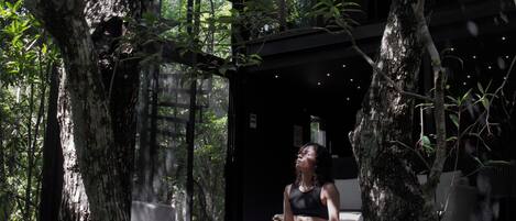 A woman sitting on a bench in a forested area with a modern building in the background.