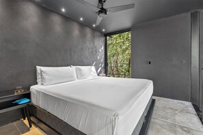 A modern bedroom with a large bed, a ceiling fan, and a window with a view of trees. - Tree60 - Jungle Villa with Private Rooftop & Wood-Hot Tub (Tulum)