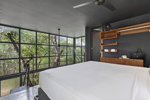Un dormitorio con un ventanal grande, una cama, un ventilador de techo y estanterías empotradas.
