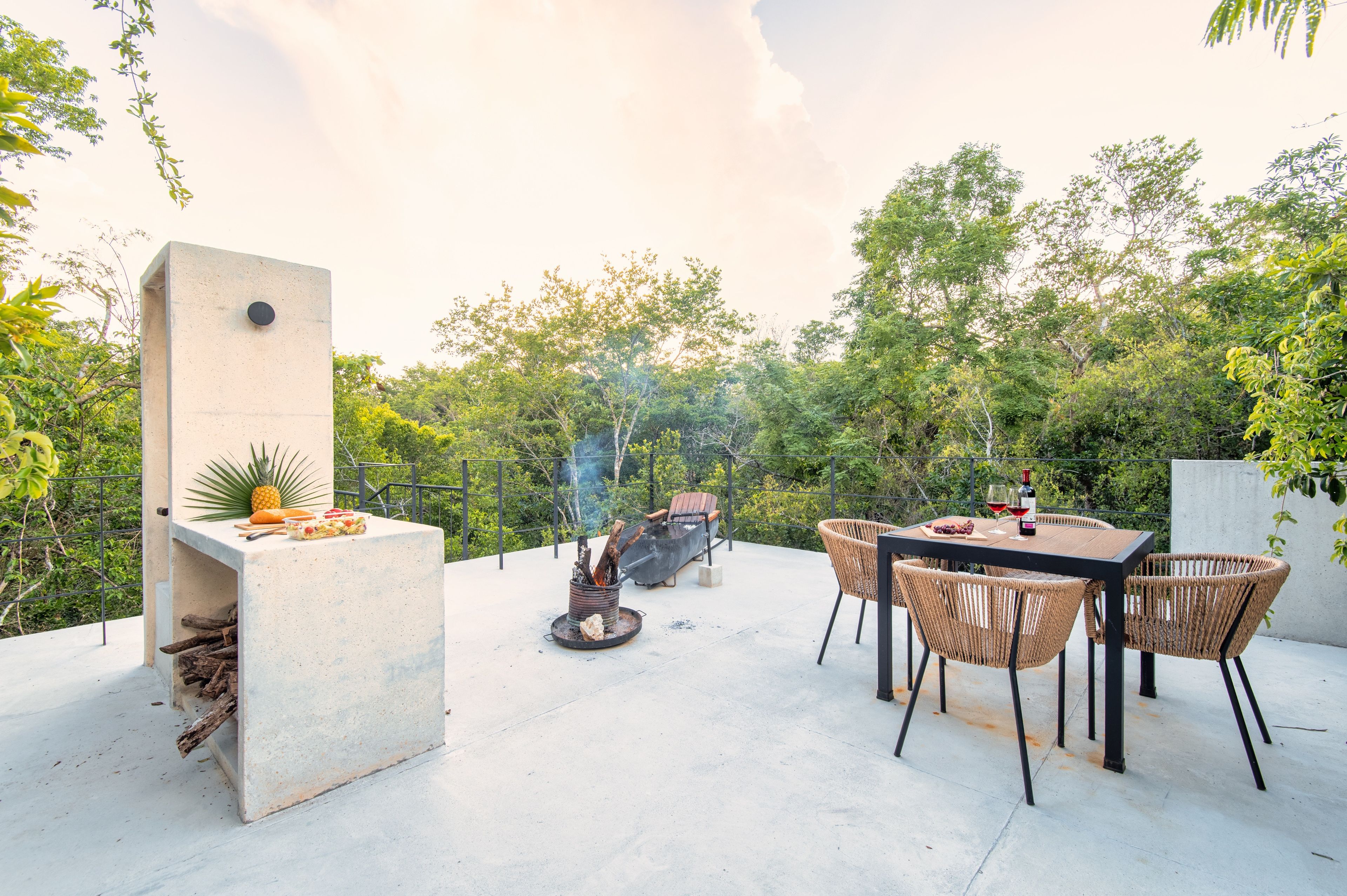 Un patio exterior con una mesa de concreto, sillas de mimbre, una parrilla y un brasero.