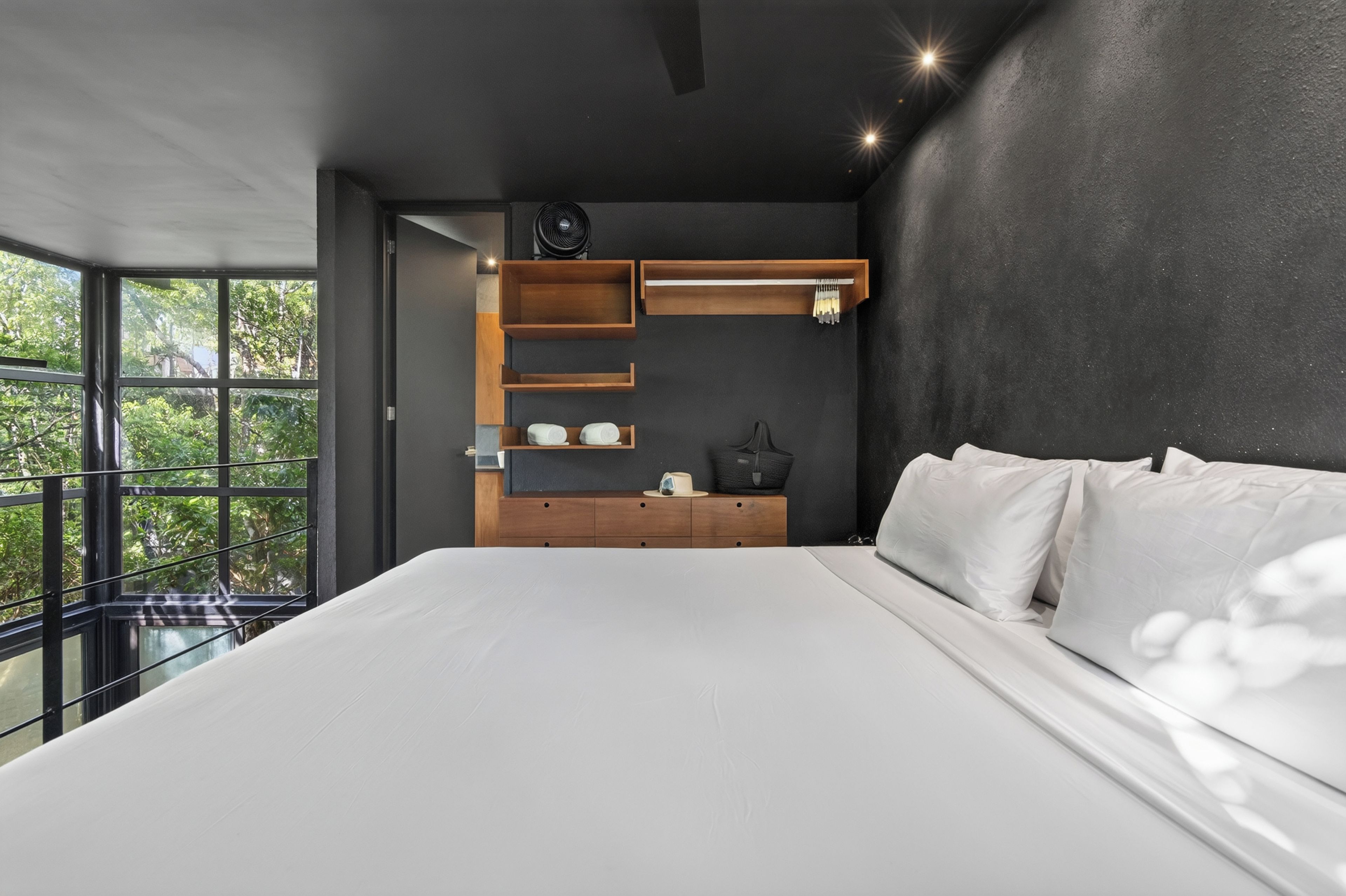 A modern bedroom with a large bed, built-in wooden shelves, and a view of greenery outside.