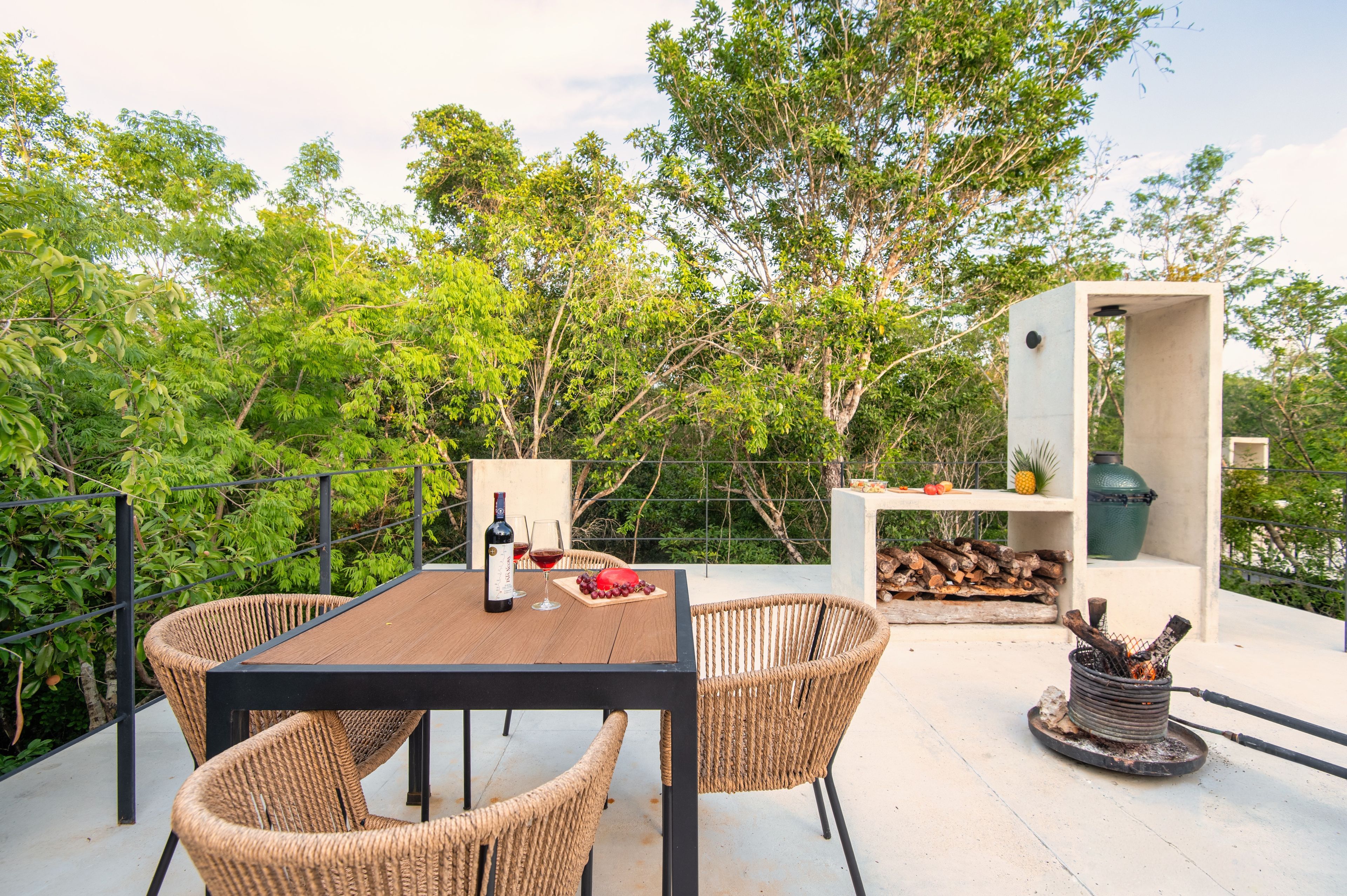 An outdoor seating area with wicker chairs, a table, a bottle of wine, and a fire pit.