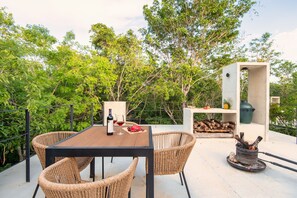 An outdoor seating area with wicker chairs, a table, a bottle of wine, and a fire pit. - Tree60 - Jungle Villa with Private Rooftop & Wood-Hot Tub (Tulum)