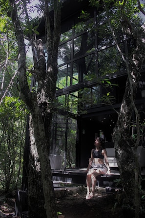 A woman sitting on a bench in a forested area with a glass structure in the background. - Tree60 - Jungle Villa with Private Rooftop & Wood-Hot Tub (Tulum)